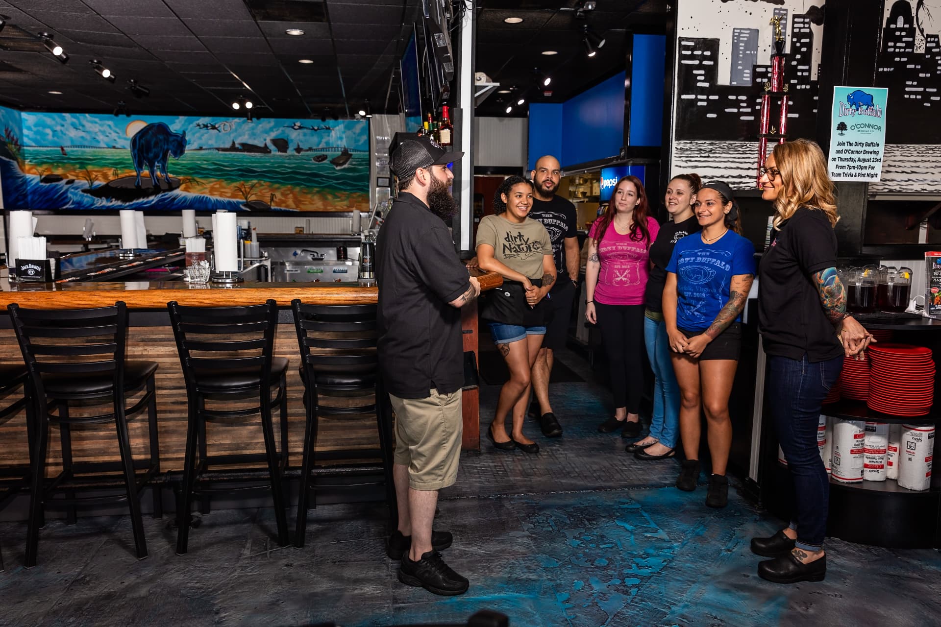 The East Beach team gathered at the bar for a pre-shift meeting under the buffalo beach mural