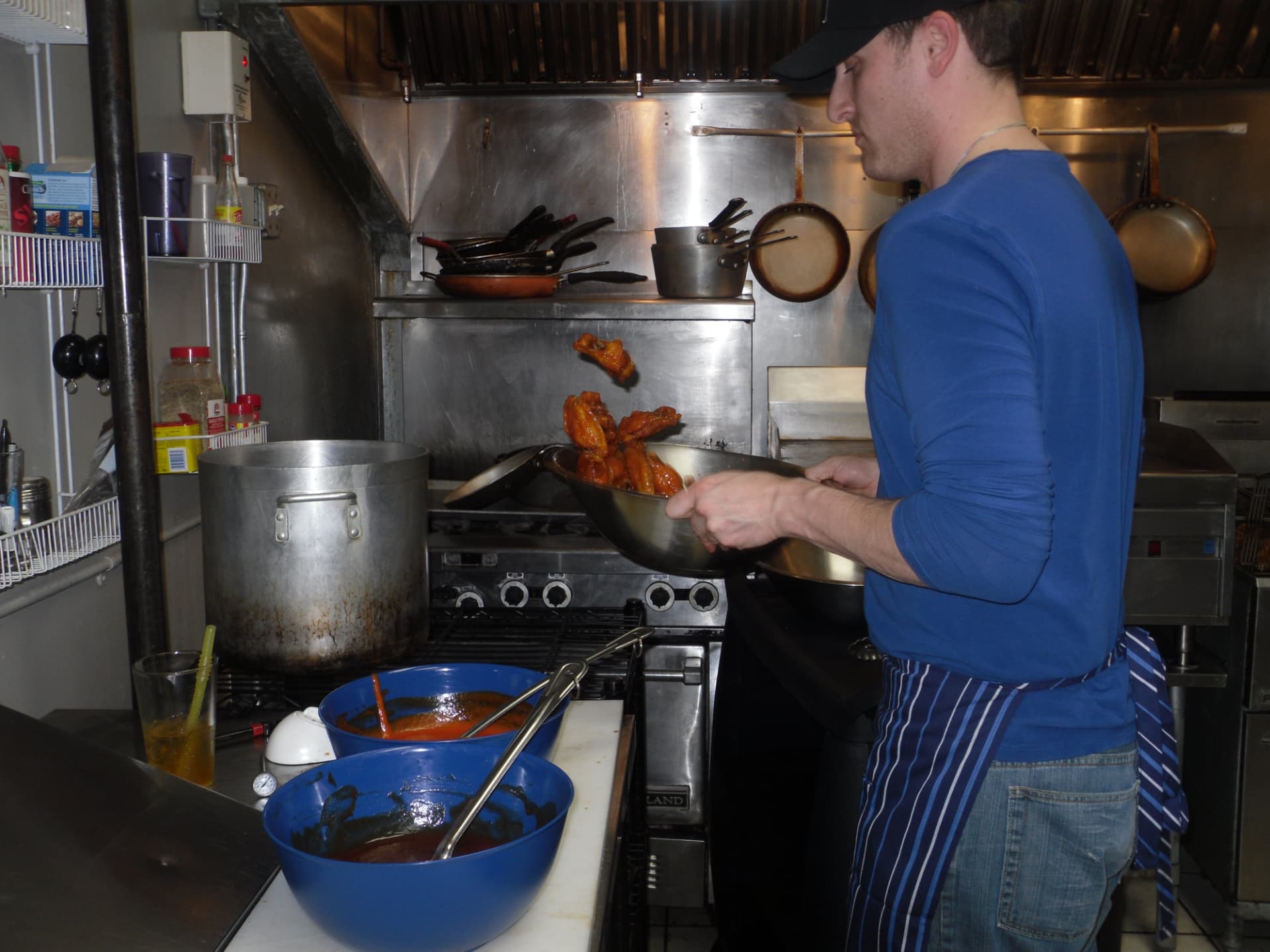 Russ Gilbert in an apron tossing wings in sauce in the original Dirty Buffalo kitchen