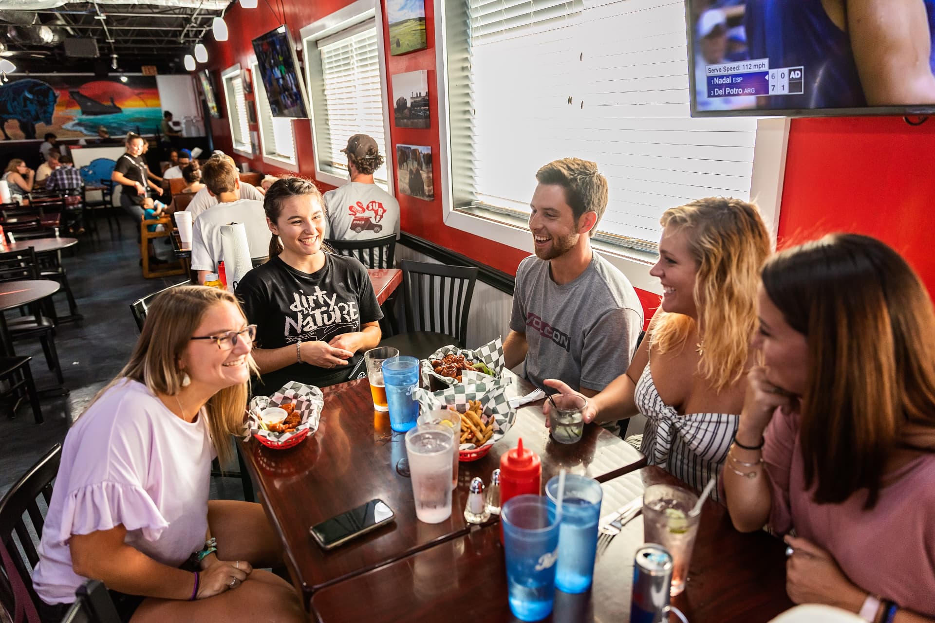 A server laughing with a table of guests over wings at The Dirty Buffalo