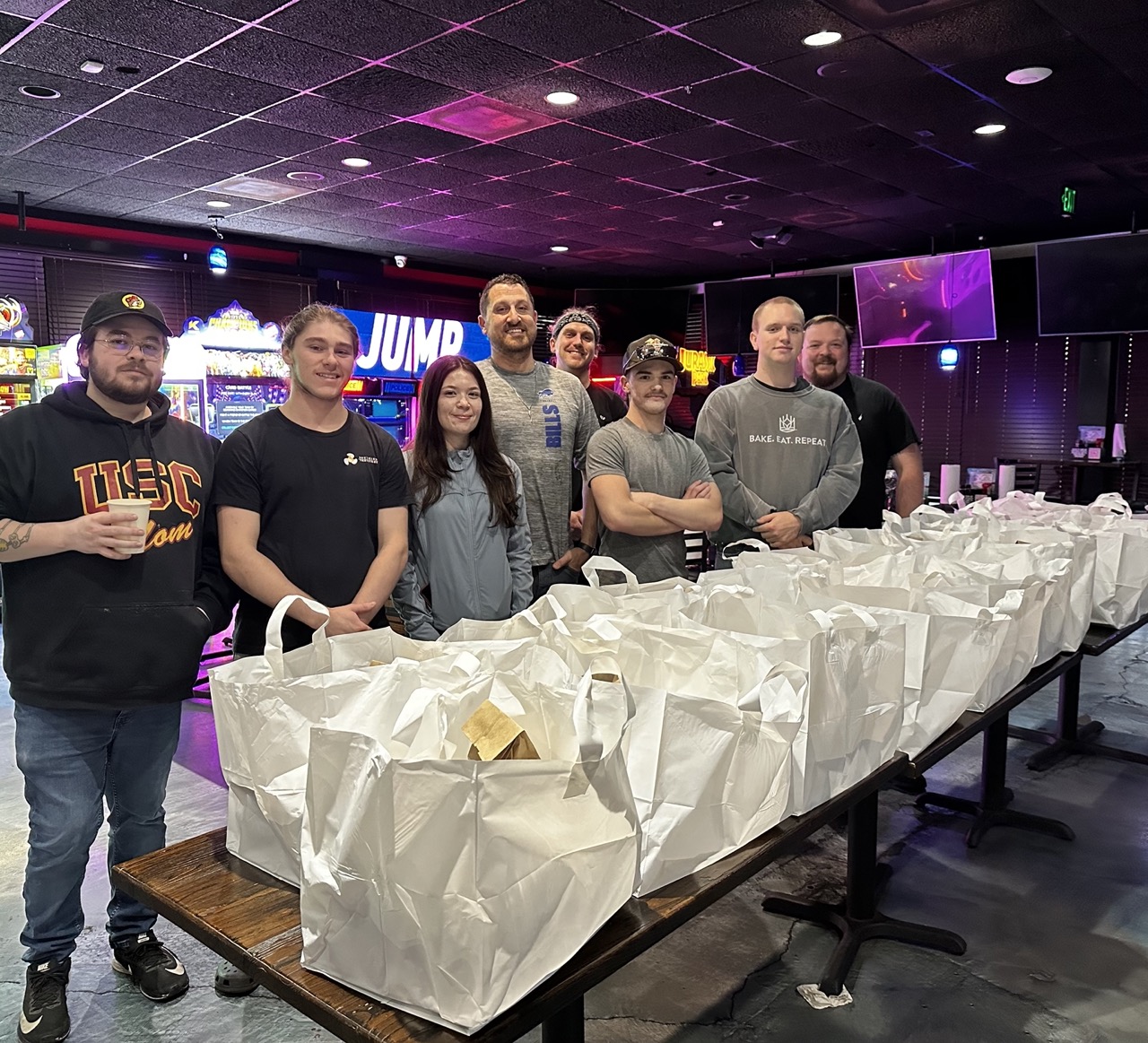 The Little Creek team standing behind rows of packed meal bags in the game room