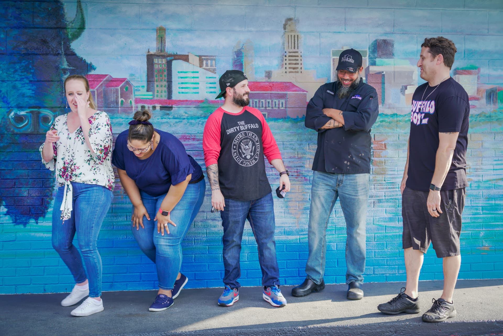 Dirty Buffalo leaders laughing together in front of the Norfolk mural