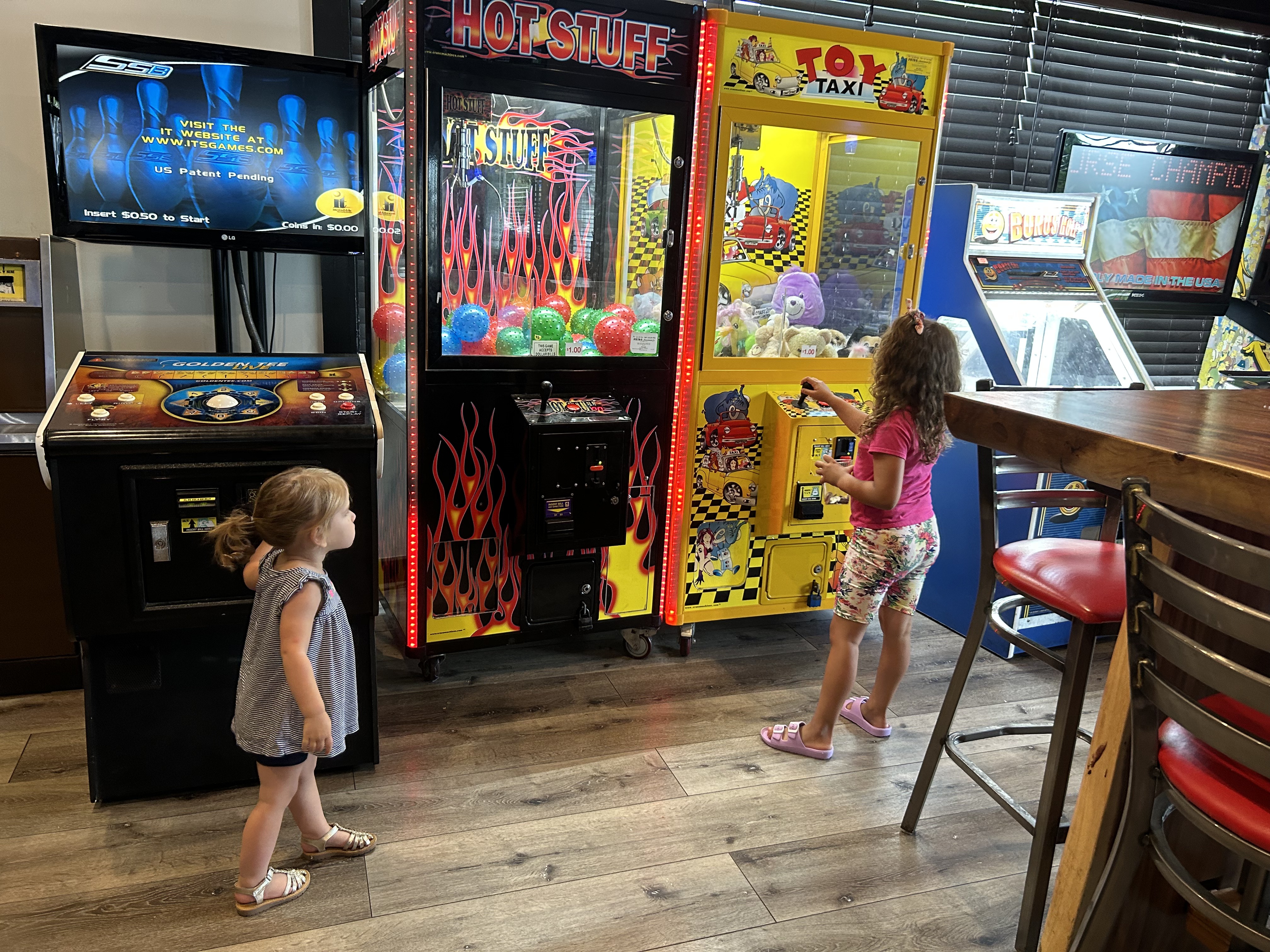 Two kids playing arcade games and the toy crane in the Princess Anne game room