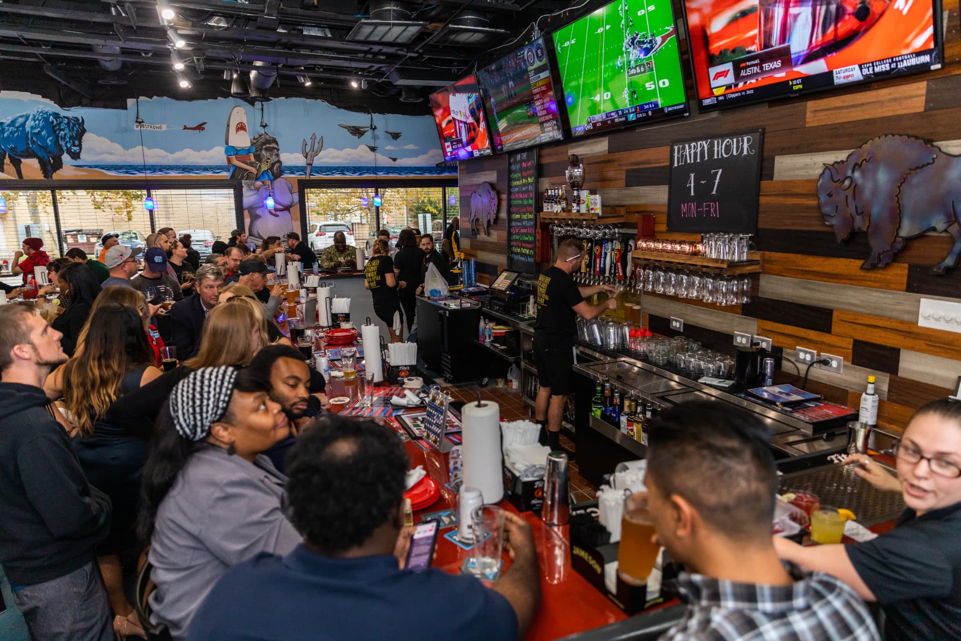 A packed bar at The Dirty Buffalo Princess Anne with games on every TV and the buffalo beach mural overhead
