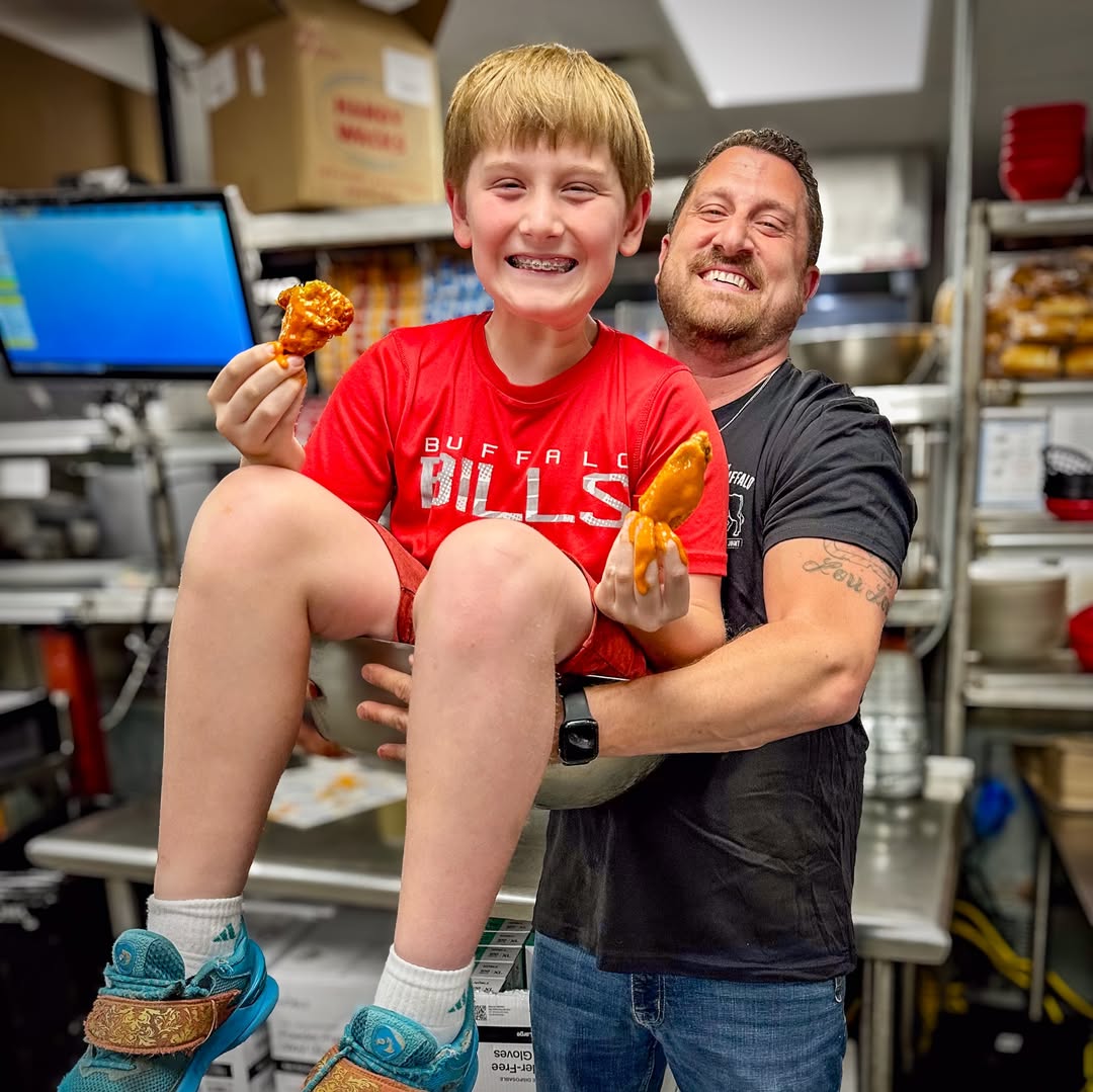 Russ Gilbert holding his son RJ, who is sitting in a giant metal mixing bowl eating wings