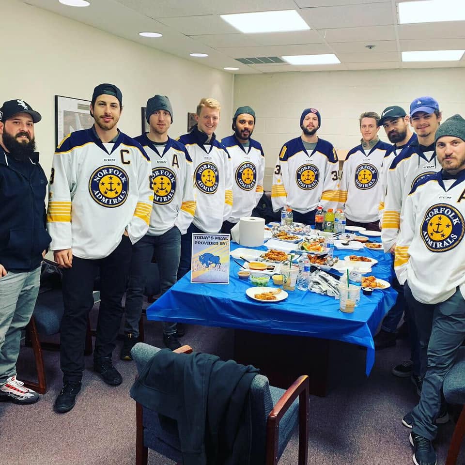 Norfolk Admirals players in jerseys around a spread of Dirty Buffalo wings