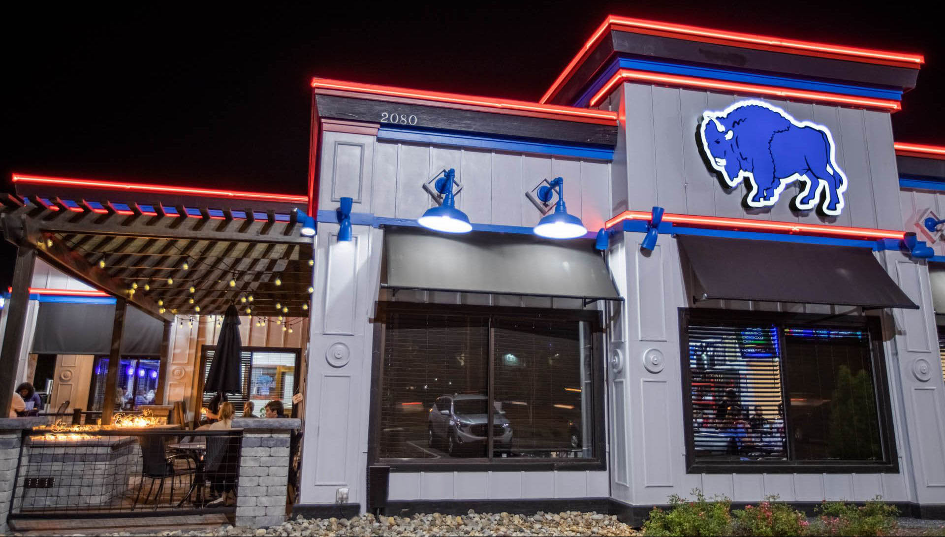 The Dirty Buffalo Princess Anne at night — blue bison sign, red and blue neon trim and a string-lit patio