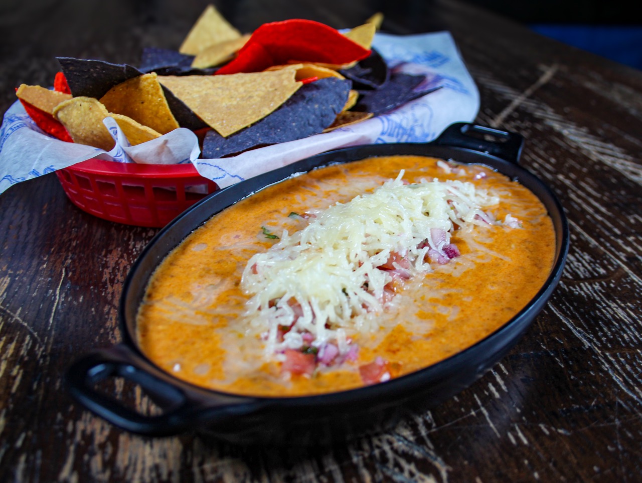 Skillet of Taco Dip topped with shredded cheese and pico, served with tri-color tortilla chips