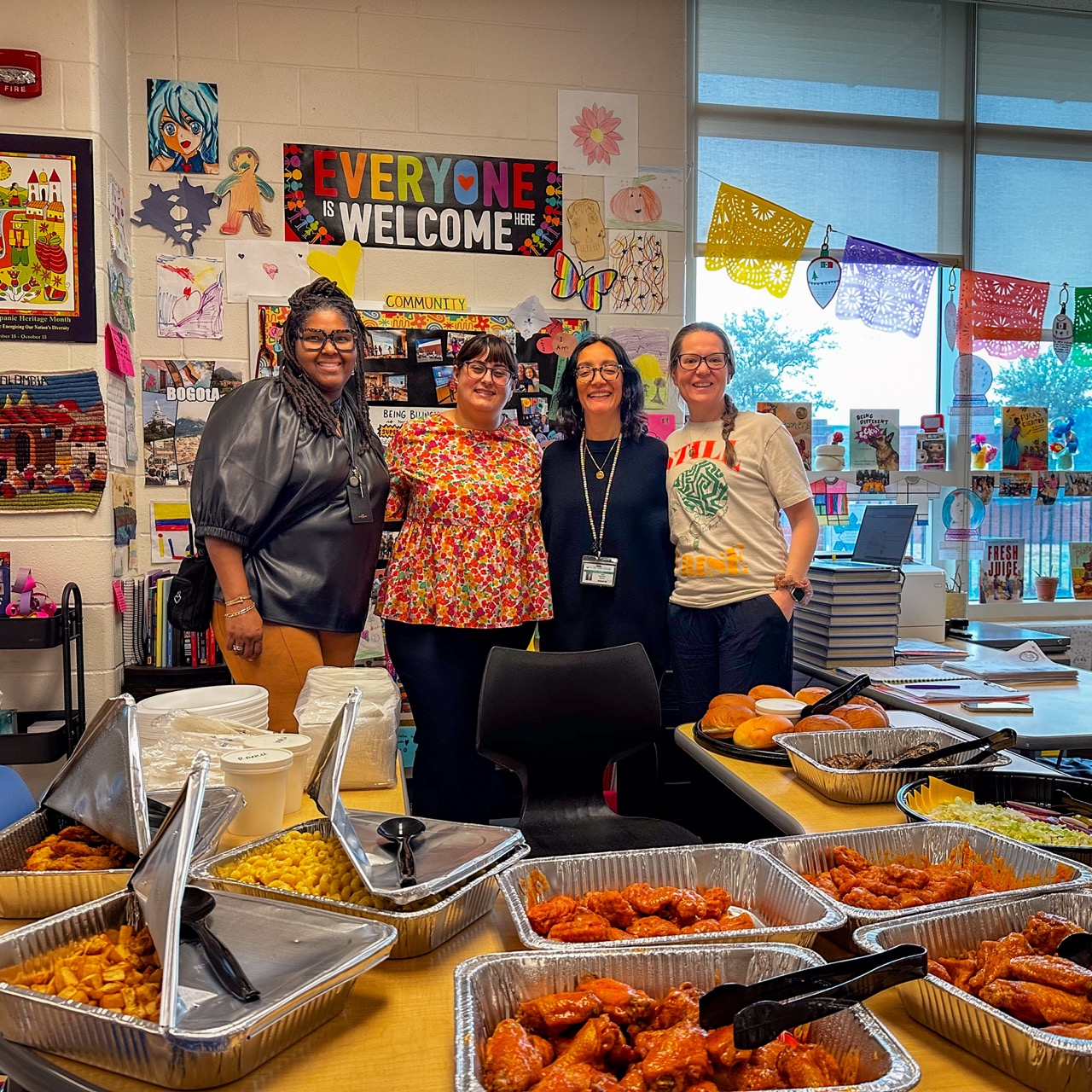 Teachers gathered around trays of Dirty Buffalo catering in a school breakroom