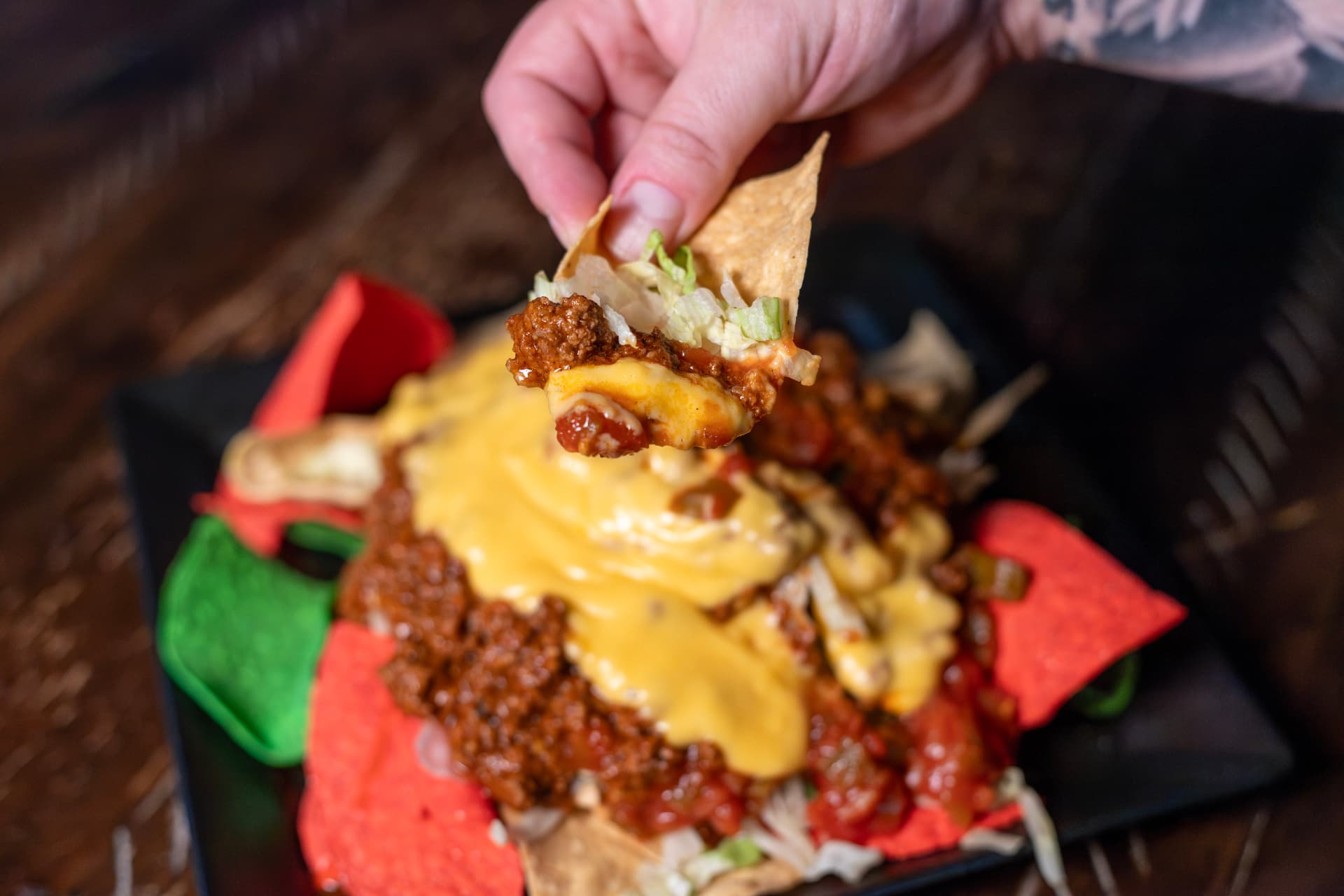 Hand lifting a tortilla chip loaded with Dirty Sauce, cheese sauce and lettuce from Dirty Nachos